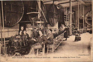 Ein Schwarz-Weiß-Foto von Frauen, die in einer Fabrik arbeiten, mit einigen sitzend und anderen stehend, mit Text unten, der 'Amer Picon - Use de Bordeaux-Bastide' lautet.