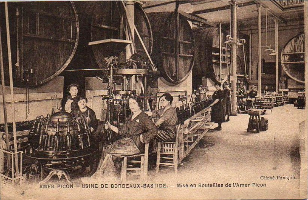Ein Schwarz-Weiß-Foto von Frauen, die in einer Fabrik arbeiten, mit einigen sitzend und anderen stehend, mit Text unten, der 'Amer Picon - Use de Bordeaux-Bastide' lautet.