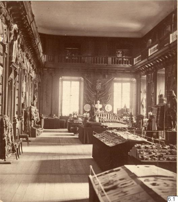 Ein altes Schwarz-Weiß-Foto eines Raumes voller Tische, Stühle, Skulpturen an den Wänden, Fenstern, Vorhängen, Geländern und anderen Gegenständen mit der Aufschrift "The Museum of Fine Arts, London" unten.