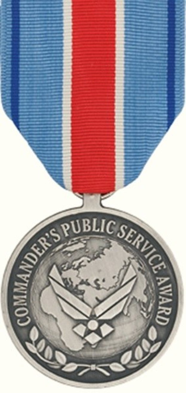 Eine silberne Medaille mit rot-weiß-blauem Band, beschriftet mit 'Commander's Public Service Award', vor einem weißen Hintergrund.