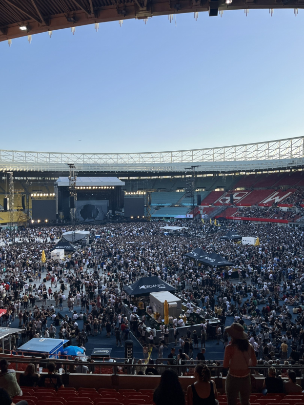 Große Menschenmenge auf Sitzplätzen und Stehplätzen in einem Stadion mit Zelten, Geländern und Deckenbeleuchtung während eines Events in der O2 Arena in London.