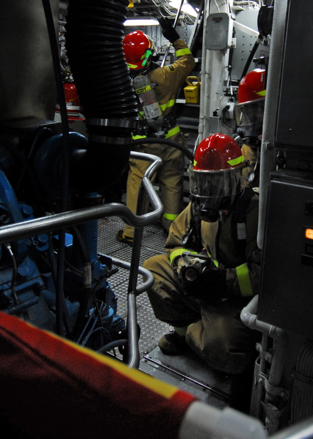 Feuerwehrleute in Schutzausrüstung arbeiten an einem Löschfahrzeug mit Equipment und einer Lampe im Hintergrund.