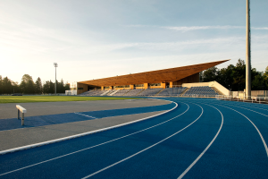 Eine blaue Laufbahn an der University of California, Berkeley, mit einer hölzernen Struktur in der Mitte, umgeben von Gras, Pfählen, Laternen und Bäumen, unter einem bewölkten Himmel.