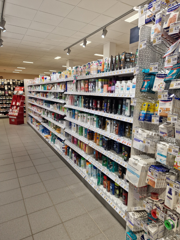 Apothekengang mit verschiedenen Medikamenten in Regalen angeordnet, beleuchtet von Deckenlampen.