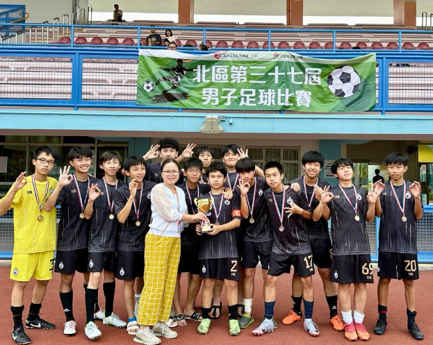 Gruppe junger Männer in Fußballtrikots, die auf einem Feld stehen und einen Pokal halten und Medaillen tragen, mit einem 'Yokohama U-16 Boys Soccer Team'-Banner im Hintergrund.