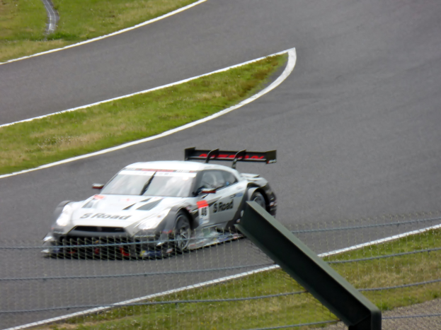 Audi R8 LMS GT3 Rennauto auf der Nürburgring 24 Stunden-Strecke, umgeben von einem Metallzaun und grünem Gras, zentral positioniert mit der Strecke, die sich vor ihr erstreckt.