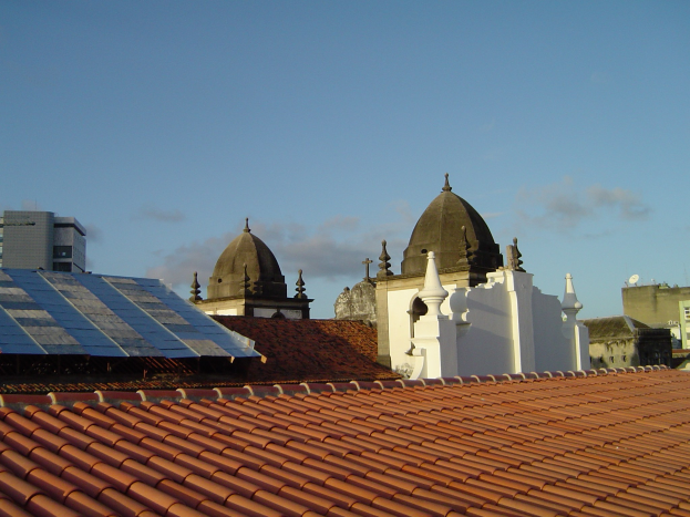 Stadtansicht mit Gebäuden im Vordergrund, einem klaren blauen Himmel im Hintergrund und Solarpanelen auf einem Dach.